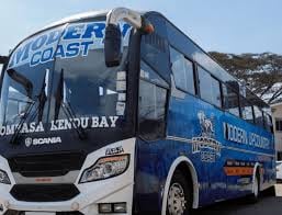 Blue and white coach bus parked on a street with hills in the background